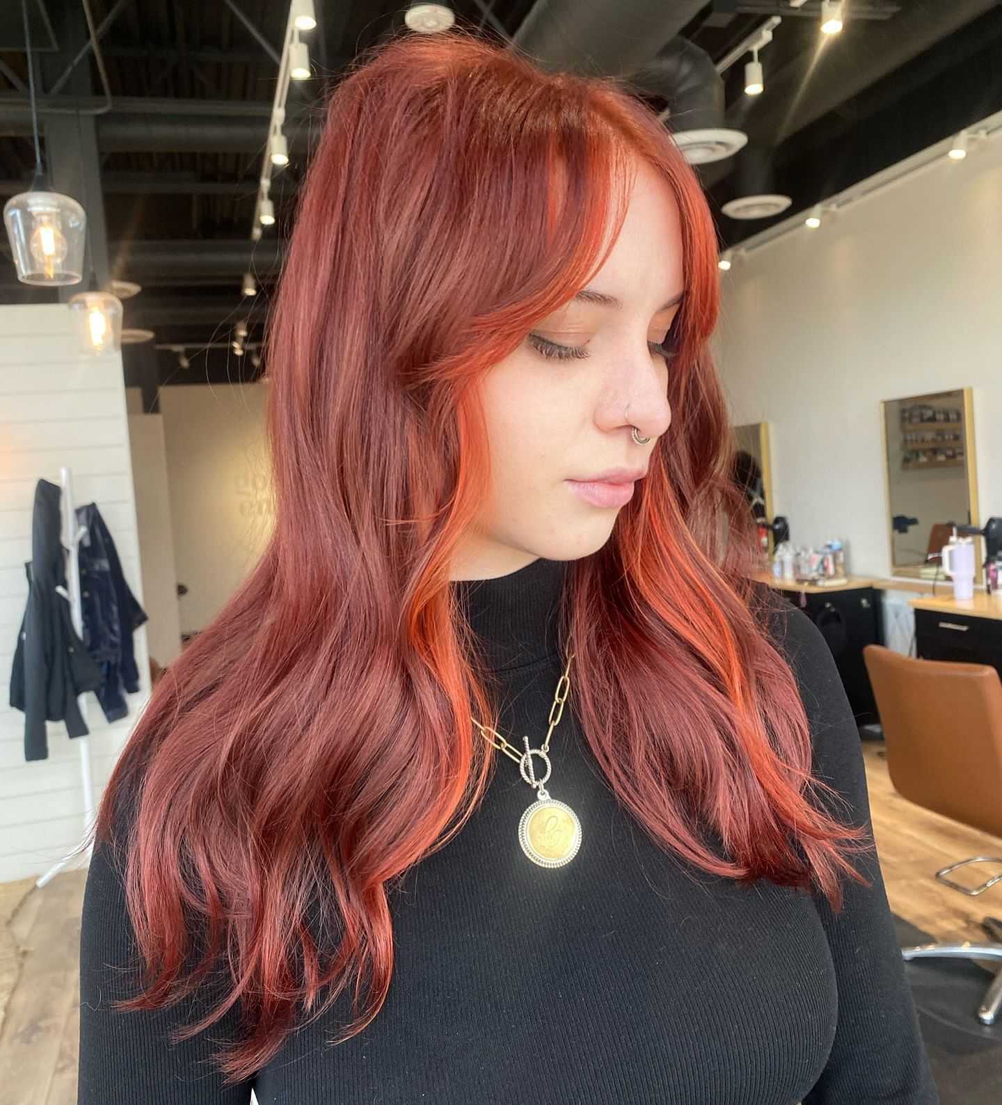 Woman with vibrant red hair and a nose ring, standing in a salon.