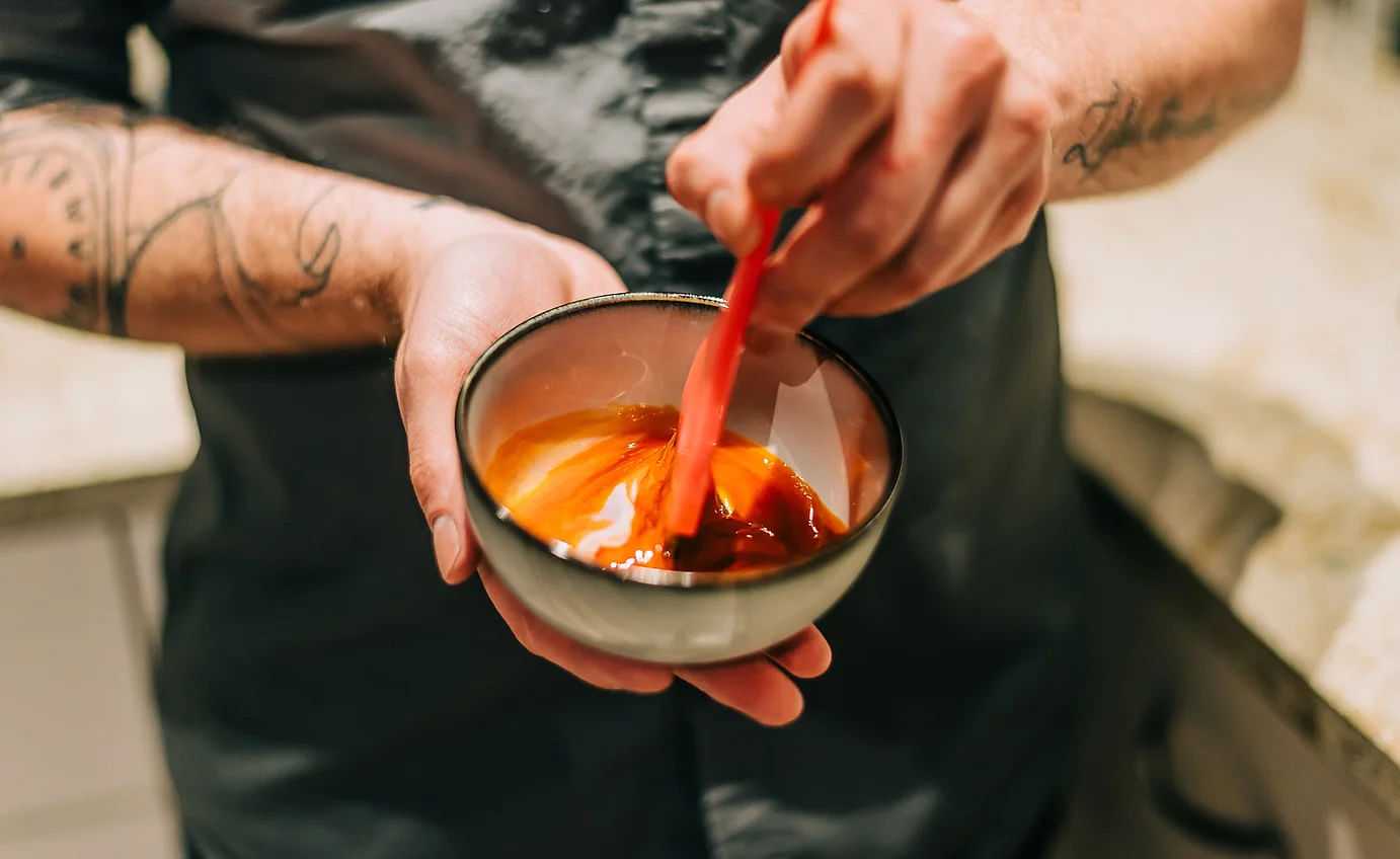 Person stirring a bright liquid in a bowl with a spatula.