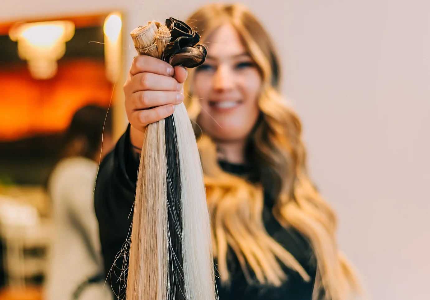 Woman smiling, holding hair extensions towards the camera.